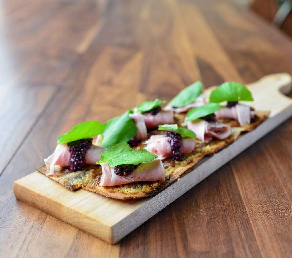 The image shows a charcuterie board on a restaurant table. The wooden board is filled with biscuits, caviar and greens. 