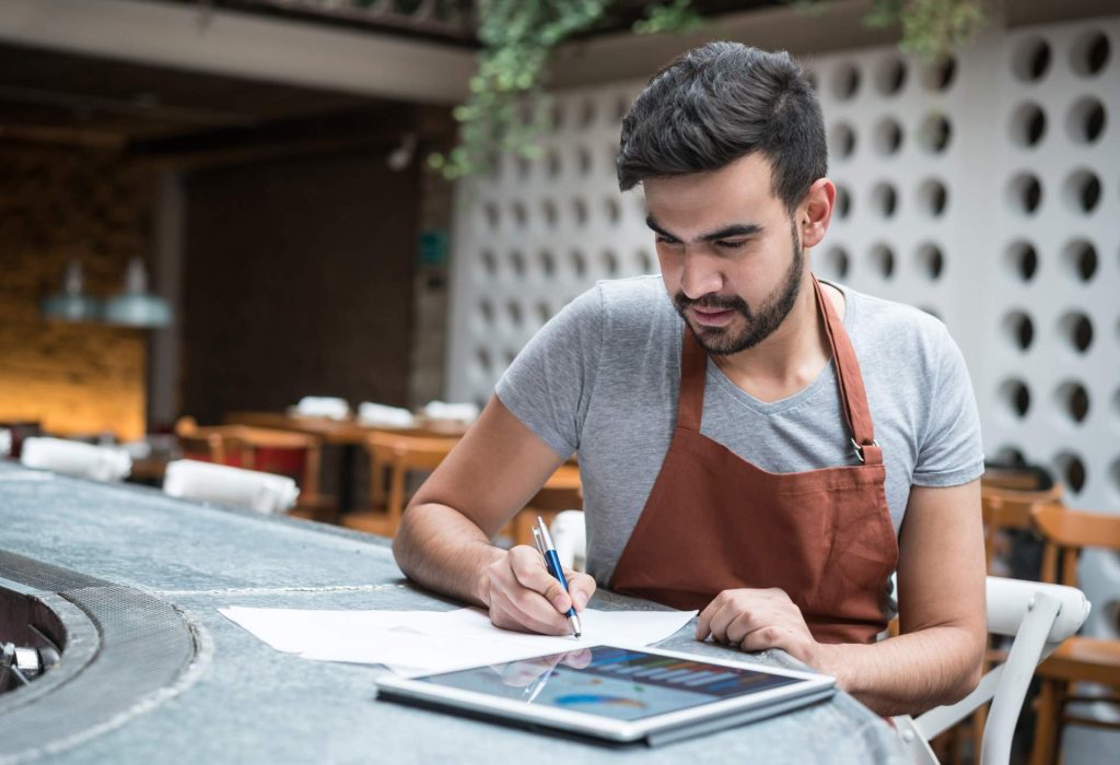 The image shows a restaurant owner working on a tablet while sitting at a table