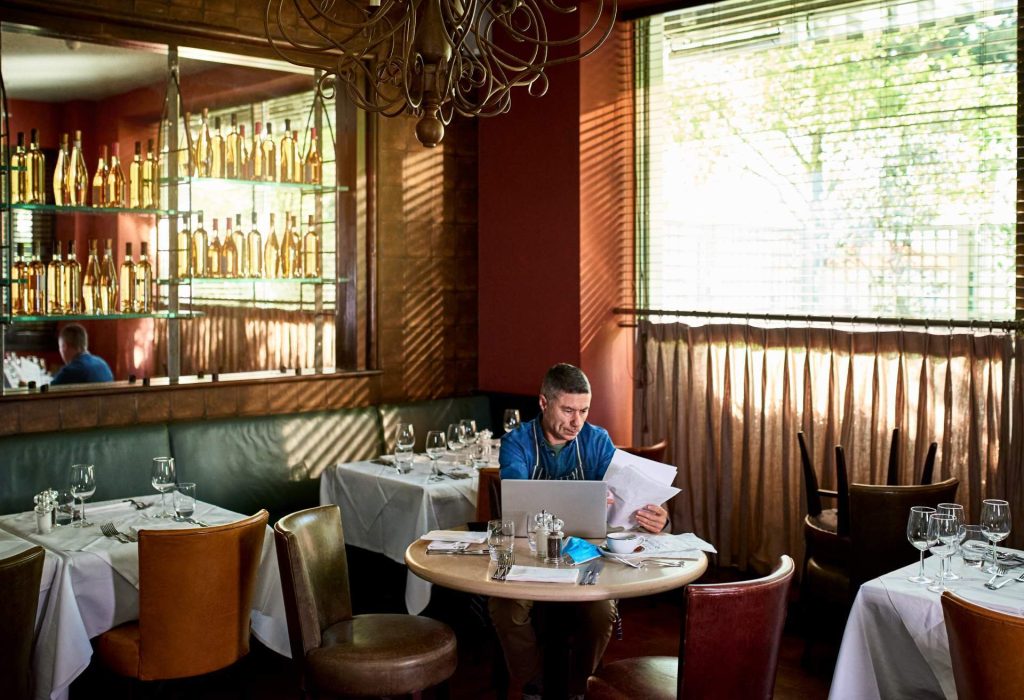 A restaurant owner looking at paperwork and working on a laptop inside their restaurant