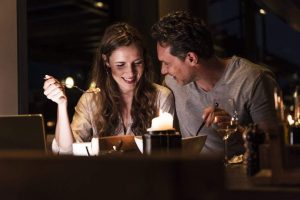 A couple eating at a restaurant and smiling at each other while having dinner