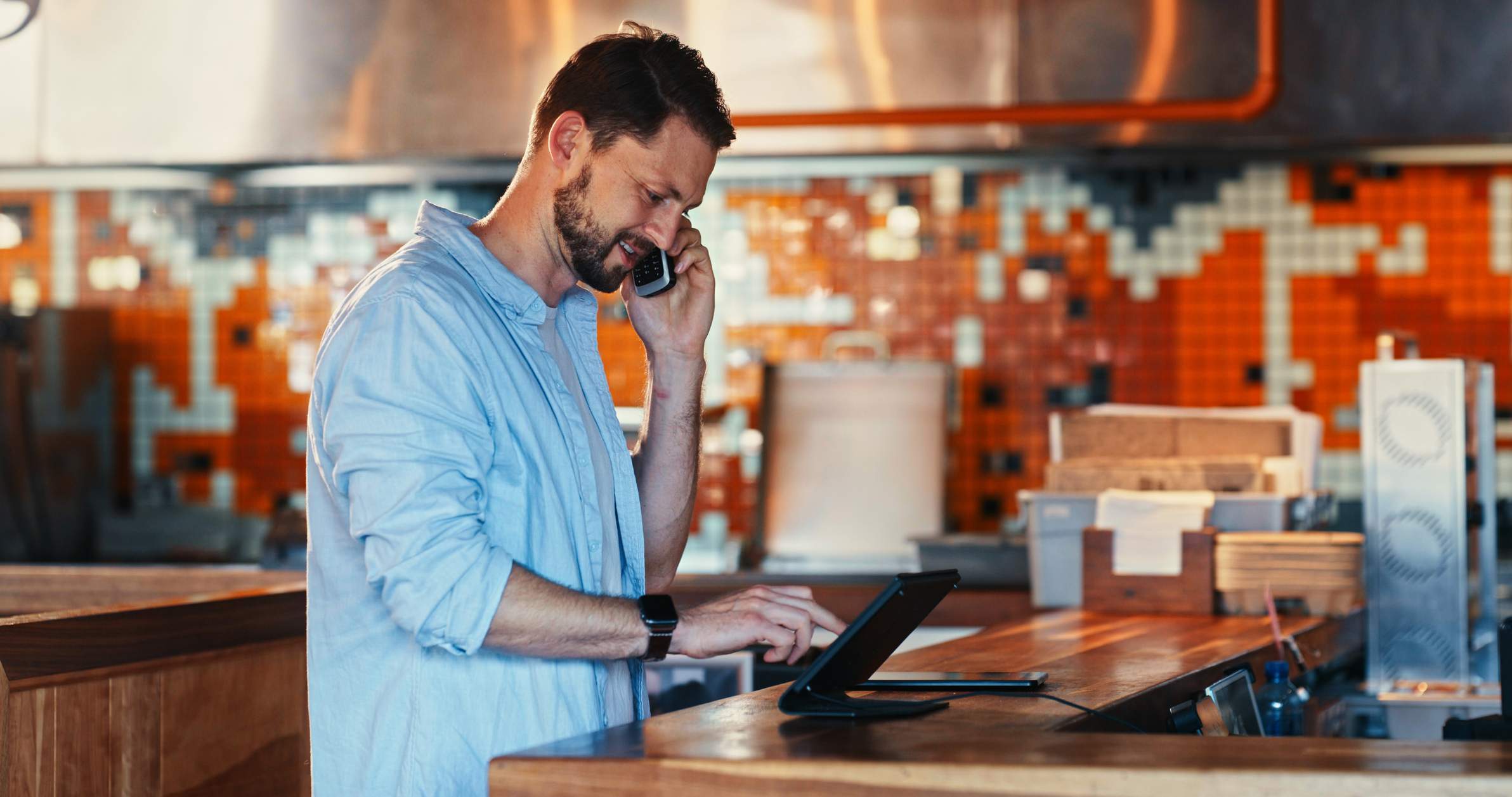 Image depicts a restaurant worker talking on the phone while using a tablet. 