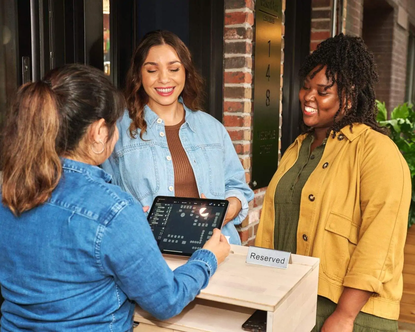 A waitress welcomes two guests at a restaurant and fills in information on a tablet at the reception.