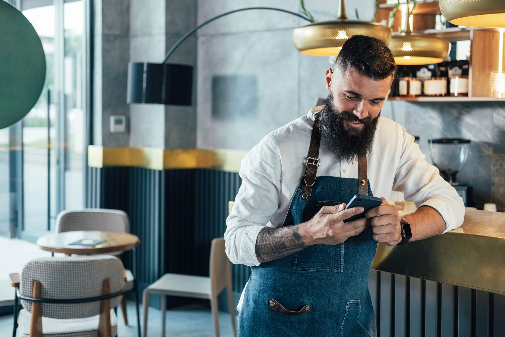 L'image représente une personne appuyée sur un comptoir de restaurant et utilisant son téléphone portable.